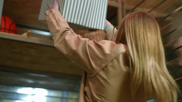 Portrait of Young Smiling Woman Putting Box on Upper Shelf in Storage Room Looking Away alt