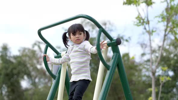 Joyful asian little girl playing exercise equipment in playground alt