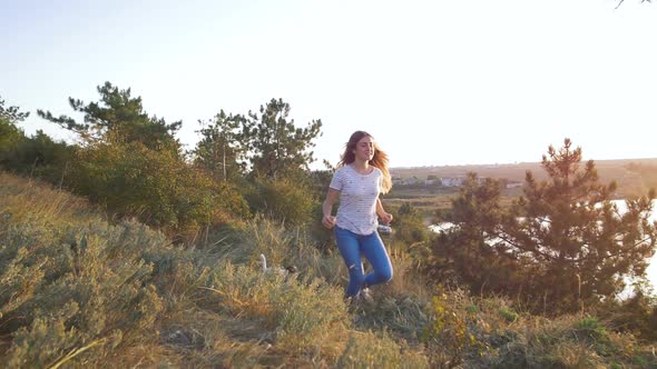 Young Attractive Woman Playing with a Dog Jack Russell in the Meadow at Sunset with Sea Background alt