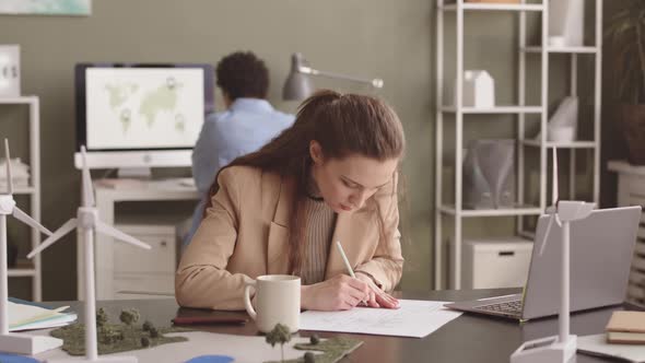 Female Engineer Drawing Blueprint of Alternative Energy Project alt