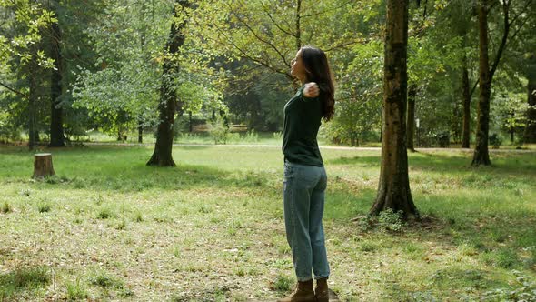 Young woman standing in park with arms outstretched