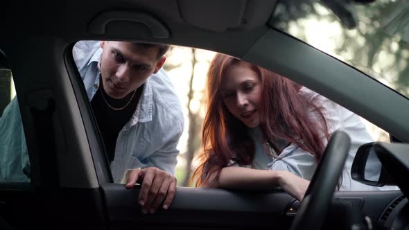Shooting From Car of Positive Young Couple Talking Looking Inside alt