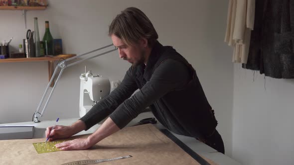 Man Tailor Draws Clothing Pattern While Working in Workshop alt