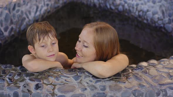 Young Woman and Her Son Relax in a Stone Bath Filled with Healing Herbal Infusions alt