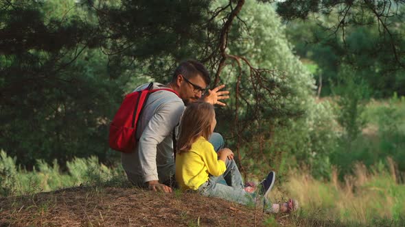 Father with Backpack and Child Sit in Forest and Look at Summer Landscape
