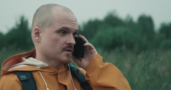 Man is Raincoat is Talking on Phone in Nature but Connection Interrupted