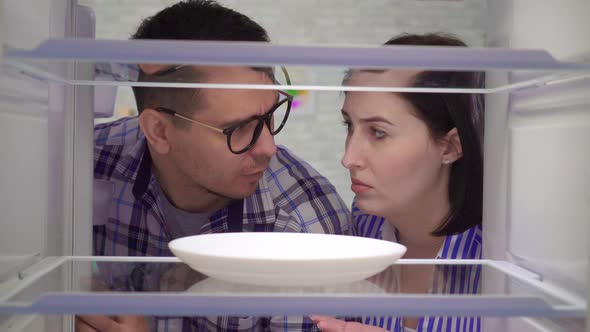 Surprised and Upset a Married Couple Looks Into an Empty Refrigerator alt