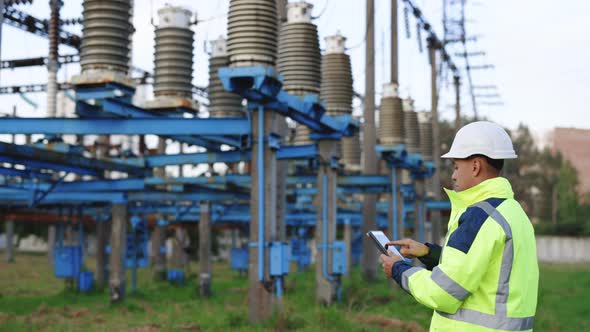 Electrical Worker Engineer Working With Digital Tablet Near Tower With Electricity
