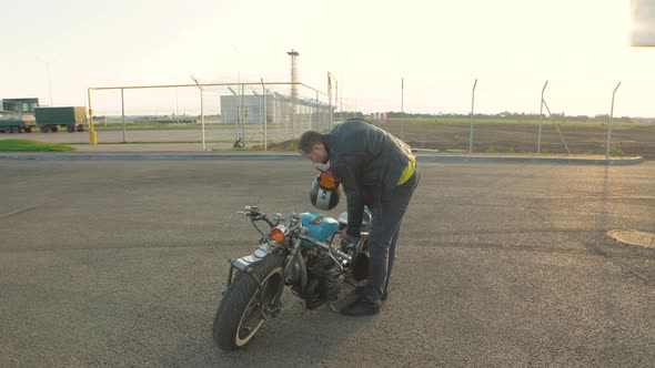 Young Man Biker with Custom Bobber Motorcycle on Street at Sunset alt