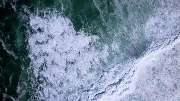 Big swell crash and runs out onto rocky coastline; aerial top-down riser alt