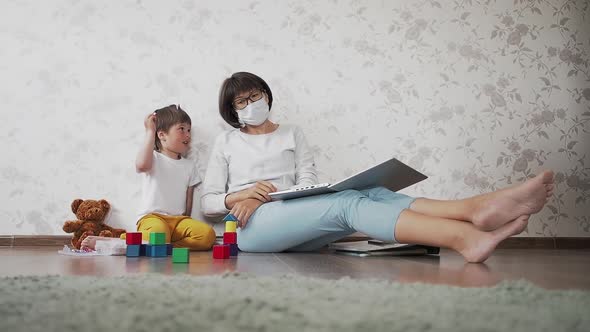 Mom and Son Sit at Home Quarantine Because of Coronavirus COVID19. Mother Works Remotely with Laptop alt