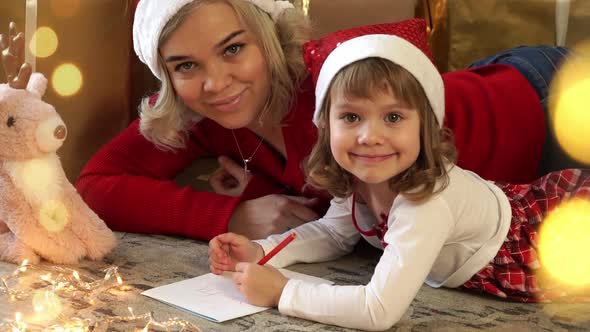 Mother and Girl Write Letter to Santa Claus on Background of Gifts