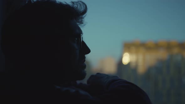 Young man with a thoughtful look sits against the background of a window and looks into the distance alt