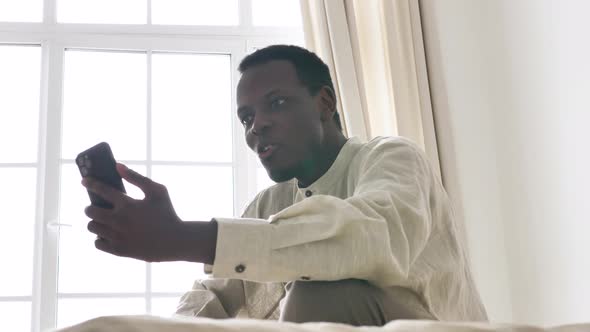 AfricanAmerican Man Talks on Phone at Videocall in Room alt