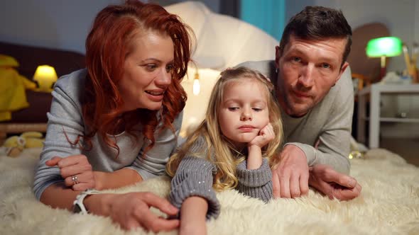Positive Caucasian Family Waving Smiling Looking at Camera Lying at Tent in Living Room alt
