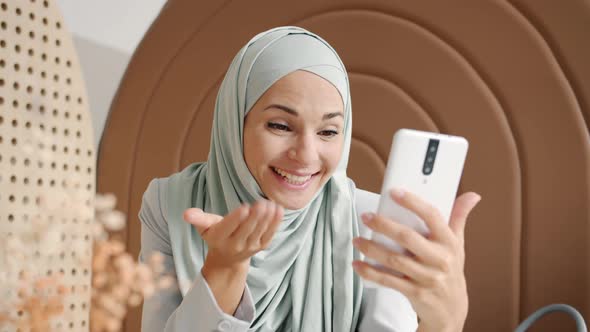 Joyful Hijabi Lady Chatting and Gesturing Making Online Video Call From Cozy Cafe alt