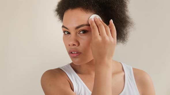 Black african american woman holding cotton pad disk cleaning face skin with cleanser tonic. alt