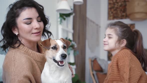 Young Mother Daughter in Knitted Sweaters are Sitting on a Bed in a Cozy Bedroom with Their Small alt