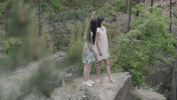 Portrait Two Beautiful Women in Short Dresses Standing on Rocky Ground with Wild Flowers and Looking alt