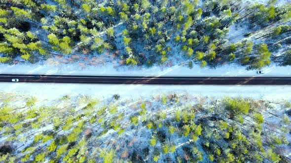 Aerial view of a winter country road in the forest with moving cars. 
