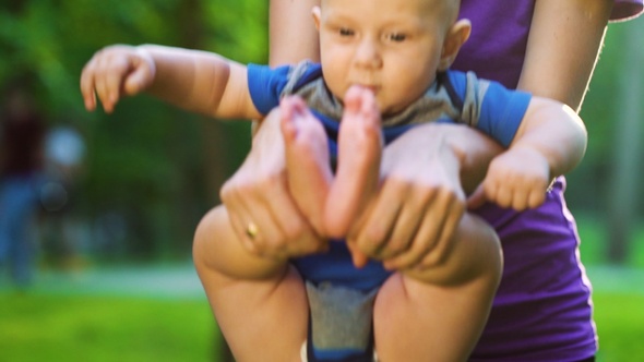 Woman holding baby and doing exercises in park alt