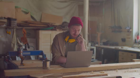 Woodworker Talking on Phone and Using Laptop in Workshop alt