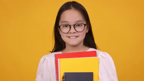 Cute Girl in Glasses and Holding Textbooks Smiling at Camera Orange Studio Background alt