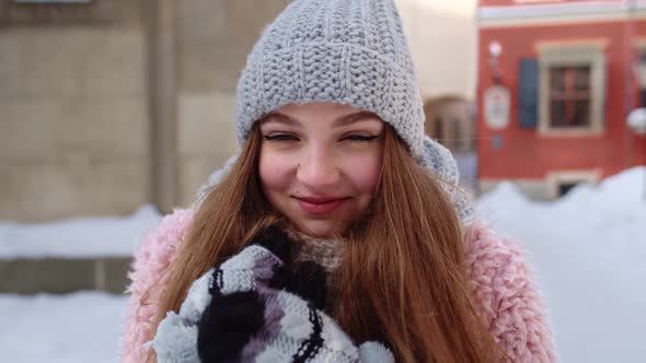 Smiling Traveler Girl Rubs Her Hands in Gloves Trying to Keep Warm in Frosty Weather on City Street alt