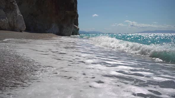 Long Sea Waves with Foam on the Beach Near the Huge Rock at Sunny Day alt