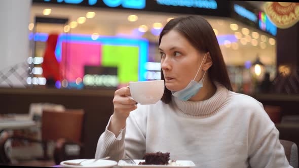 Woman with Deflated Protective Mask Drinks Coffee in a Cafe in a Shopping Mall
