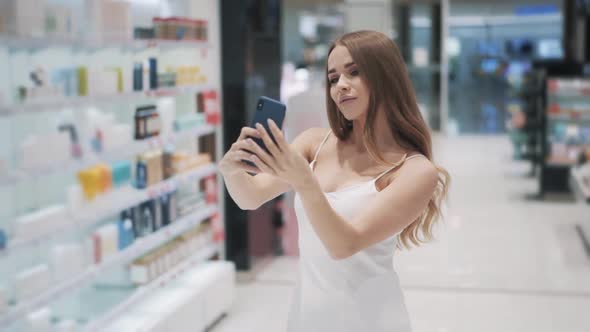 Charming Young Caucasian Woman in a White Dress Makes Selfie Using Smartphone alt