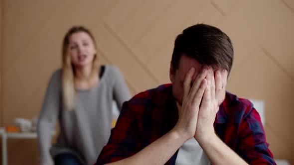 Man Covers Face Red From Tears with Hands While Sitting on Bed While Wife Swears at Him Front View alt