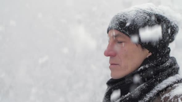 Calm Man in a Black Scarf and Hat Stands Under the Snow