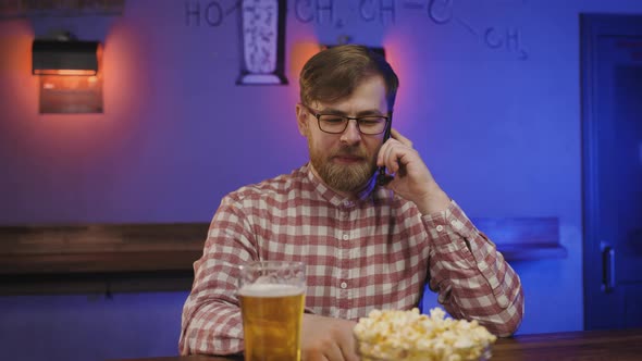 Portrait of Handsome Man with Beard and in Glasses Making Mobile Phone Call in Pub