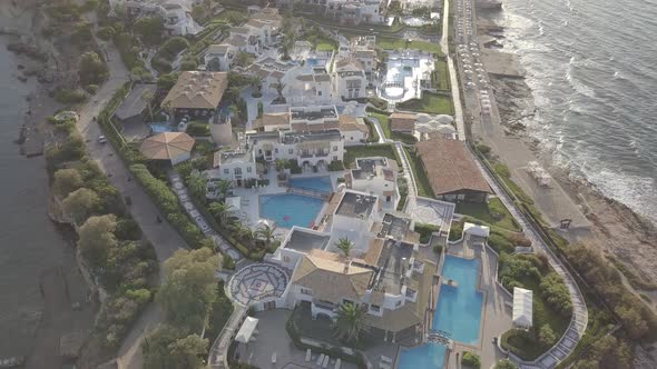 Aerial view of resort hotel with swimming pool on rocky seashore foaming waves on beach Crete Greece