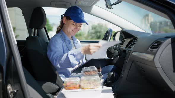Young Girl Driver Works As Courier in Food Delivery Service From a Supermarket or Restaurant Sits in alt