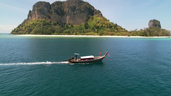 aerial drone parallel with a tourist at the front of a thai longtail boat motoring through the blue alt