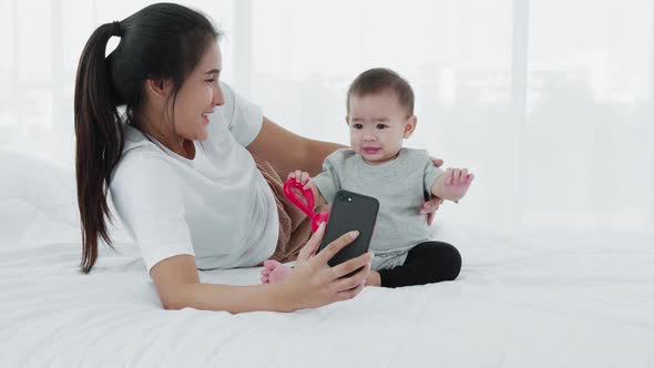 Asian mother and baby use smartphone selfies together on bed, Slow motion