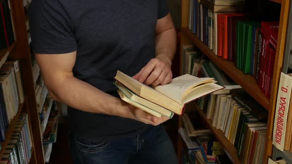 Man Standing In The Library And Turning The Book Pages