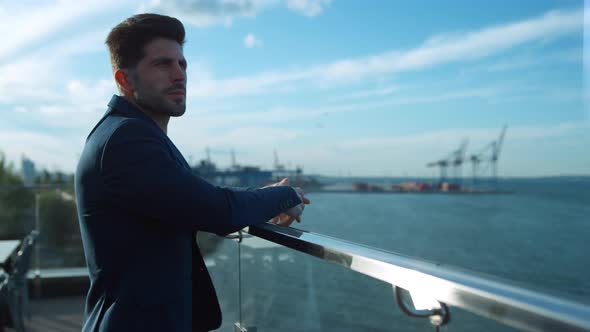 Confident Businessman Rest Balcony in Morning Sunlight at Sea Port Cranes View alt