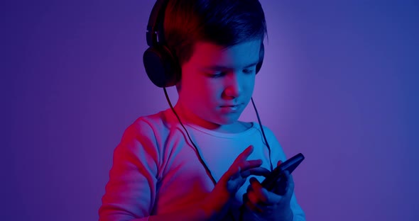 Child With Headphones Playing Game on Mobile Phone in Neon Lights 