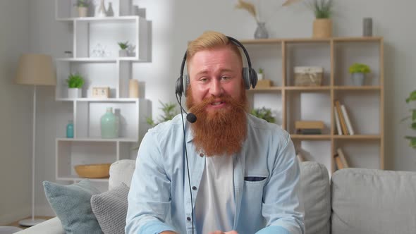 Young Redhead Man in Headphones Looks at Camera Makes Speech Negotiate Use Video Conference App and alt