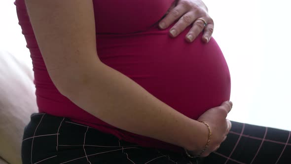 Young beautiful pregnant woman sit down at sofa at home  and touching sweetly her belly