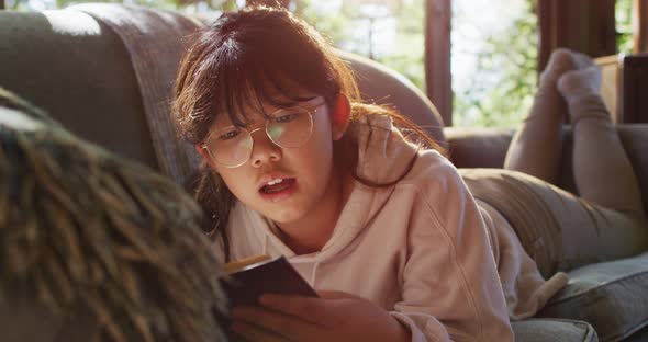 Asian girl smiling while reading a book while siting on the couch at home alt