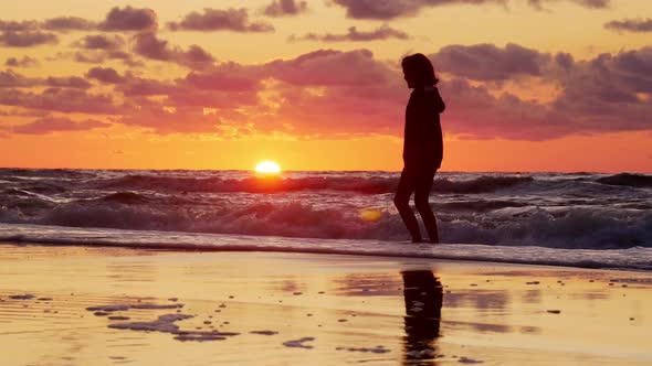 Girl Walking in Shallow Water on Sandy Beach at Sunset.