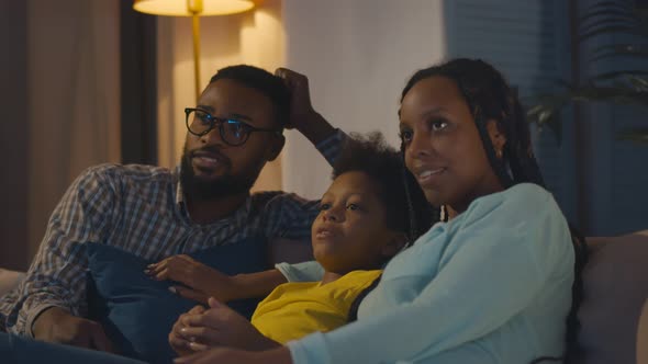 Cheerful Afroamerican Family with Kid Resting on Couch Talking and Watching Tv in Evening alt
