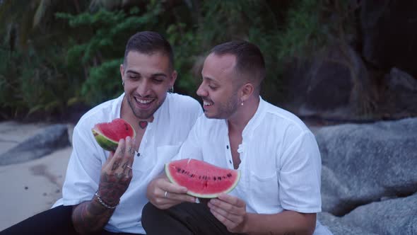 Two Male Young Gay Guys Enjoy Their Honeymoon Vacation on a Tropical Island Eating Watermelon on the alt