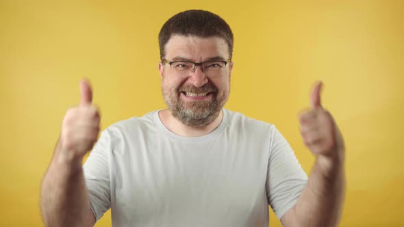 Caucasian middle-aged man in glasses with a beard showing thumbs alt