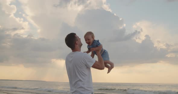 Father Throws Up His Toddler Son Into the Air at the Sea Coast alt