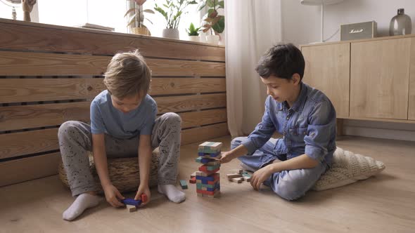 Two Boys Brothers Are Building a Tower From Wooden Blocks Sitting on the Floor alt